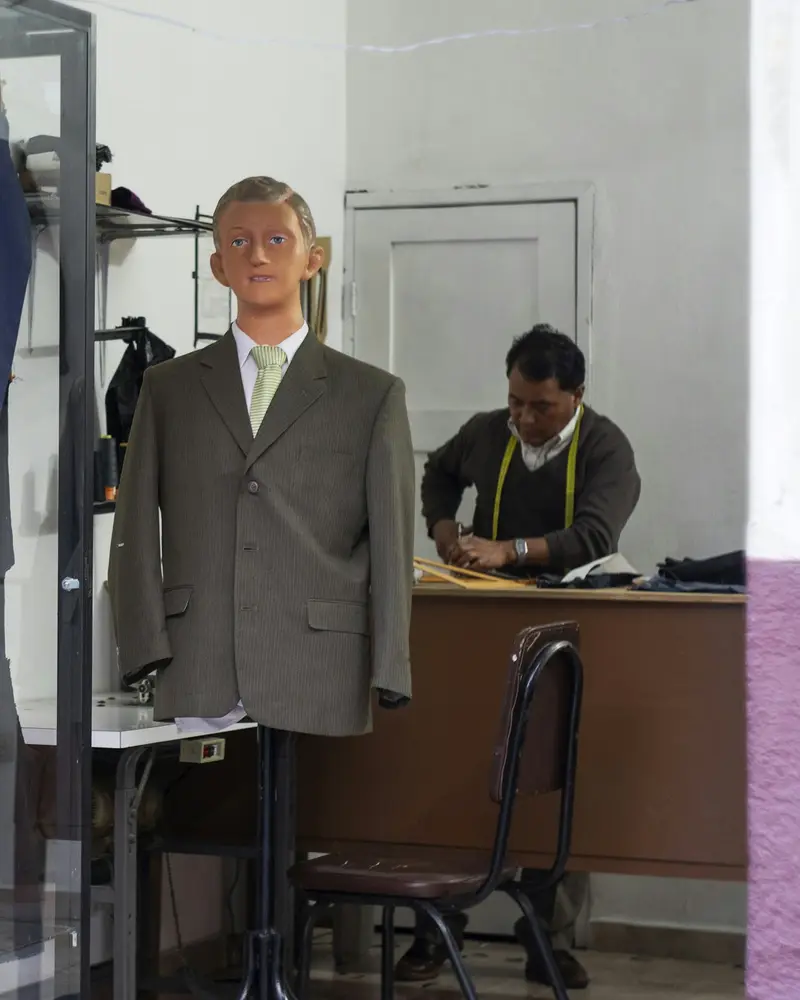 A tailor working at a bench behind a suit jacket on a stand