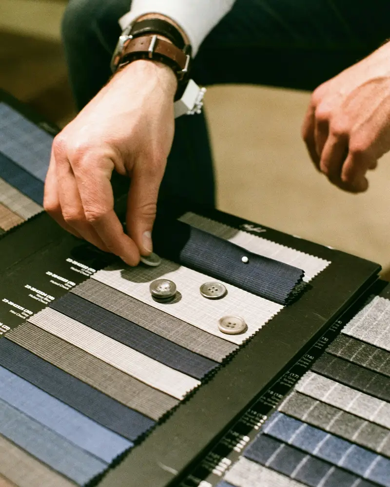 A hand choosing between rows of grey and blue suit cloth samples
