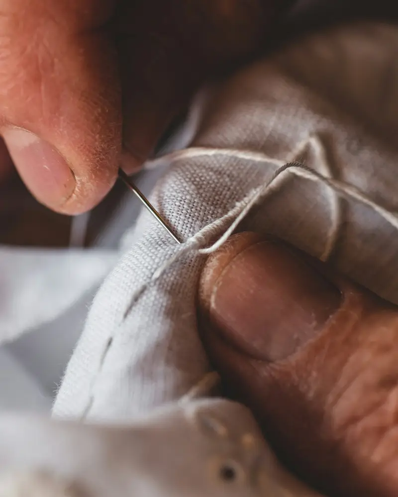 Close-up of hands sewing white fabric with a needle and thread