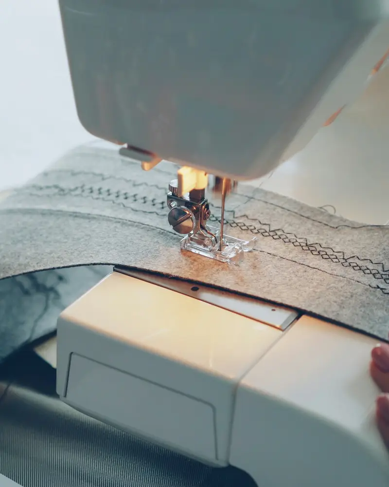 A sewing machine stitching a seam on grey fabric