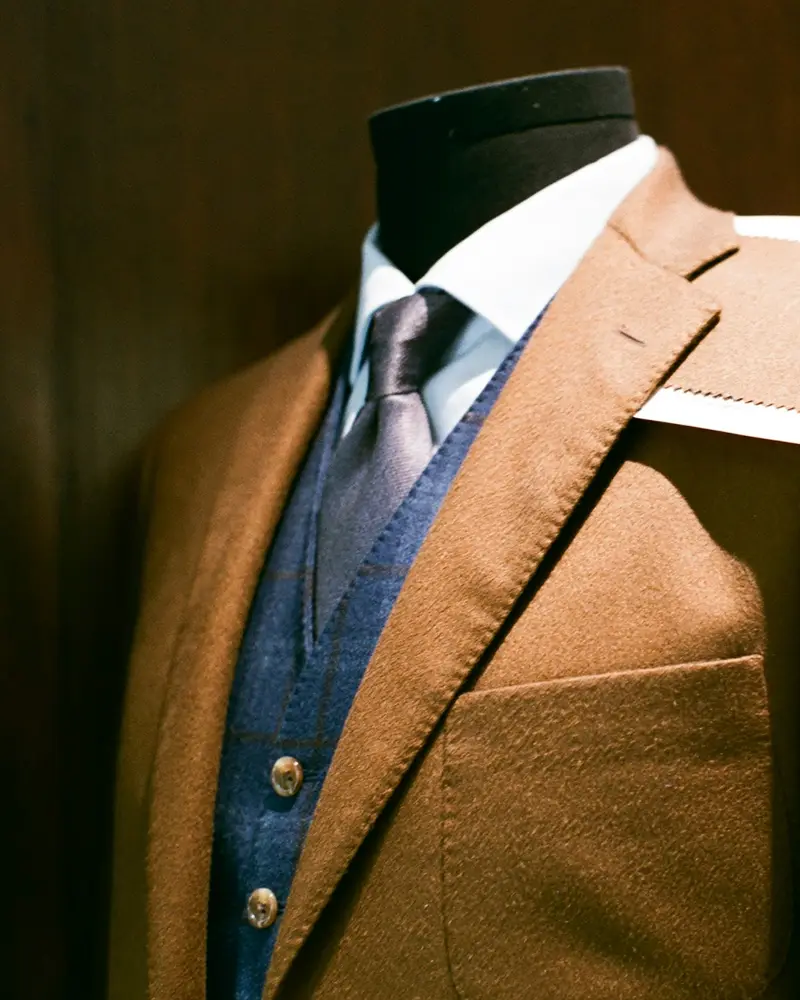 A tan wool jacket on a tailor's dummy with a cloth swatch on the shoulder