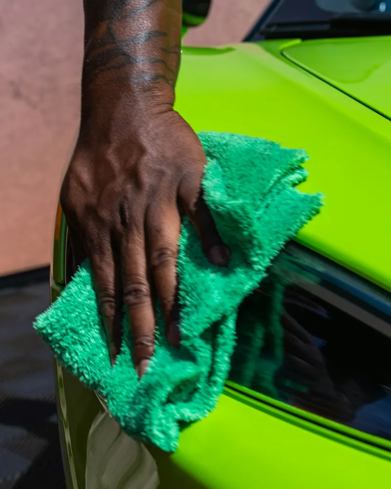 A hand wiping a green car by the headlight with a microfibre towel