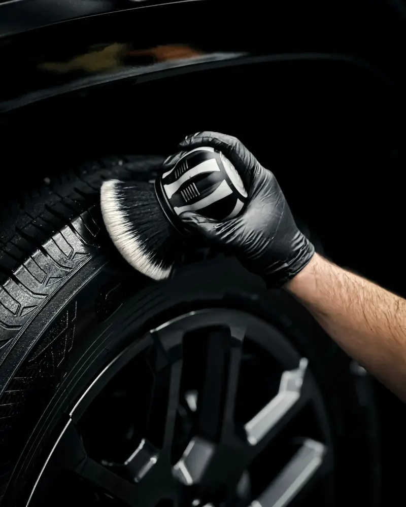 A gloved hand cleaning a tyre wall with a soft brush