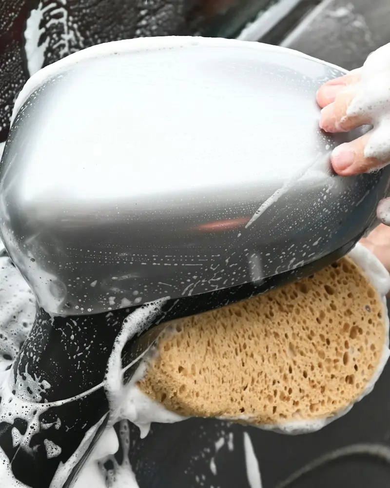 A soapy sponge being wiped over a door mirror