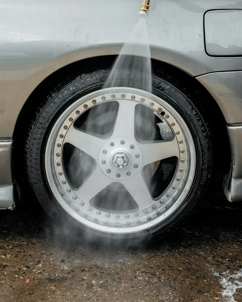 A pressure washer rinsing a silver alloy wheel