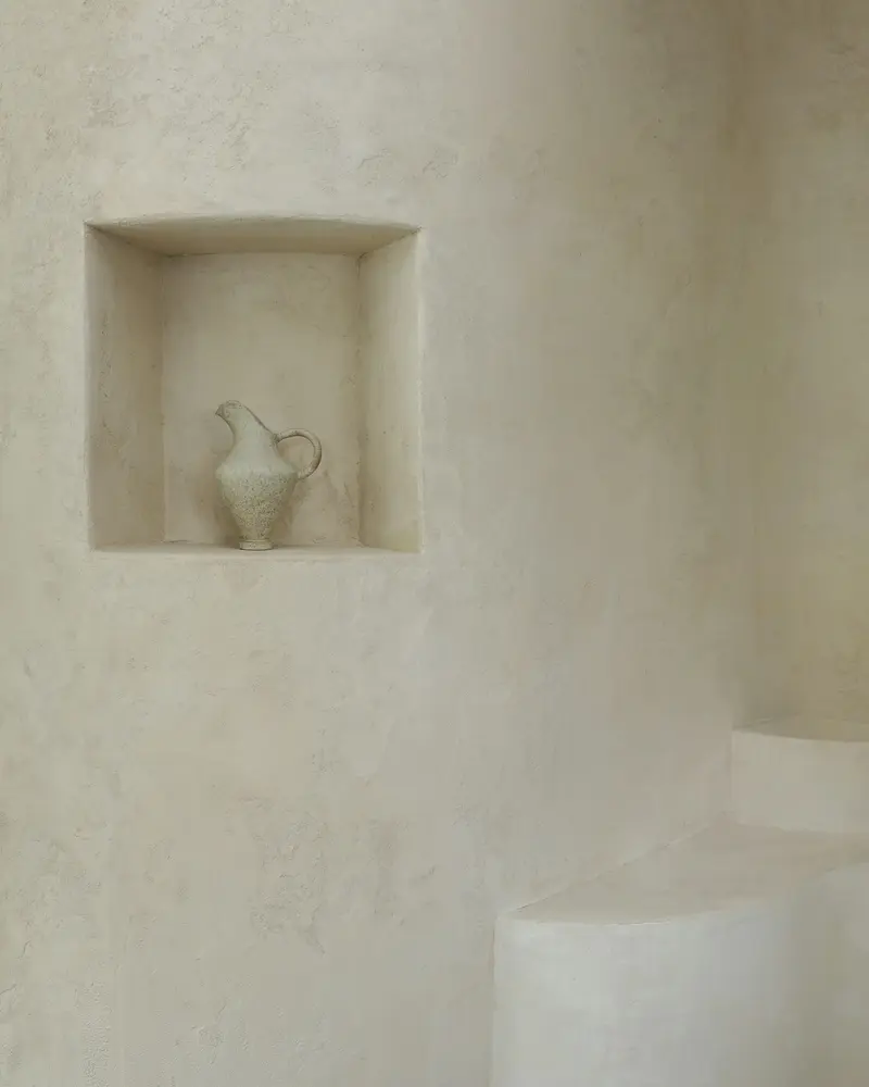 Soft white lime plaster bathroom with a recessed niche holding a jug